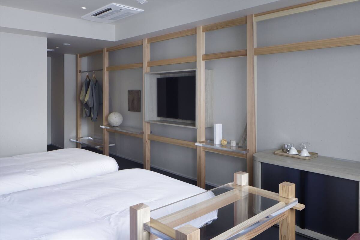 Una habitación de hotel moderna con una cama grande, un separador de vidrio, un televisor montado y un estante pequeño con artículos de tocador.
