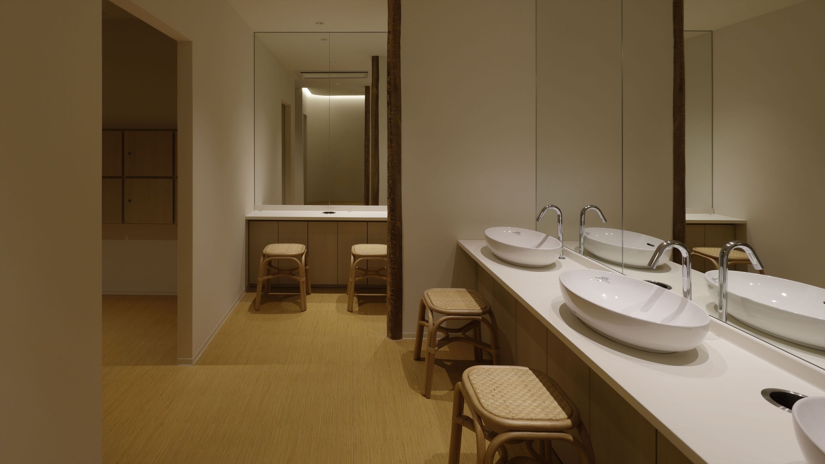 Une salle de bain moderne avec deux lavabos, un grand miroir et trois tabourets.