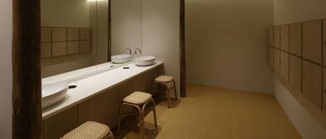Une salle de bain moderne avec un long meuble-lavabo, deux tabourets, un grand miroir et des casiers en bois.