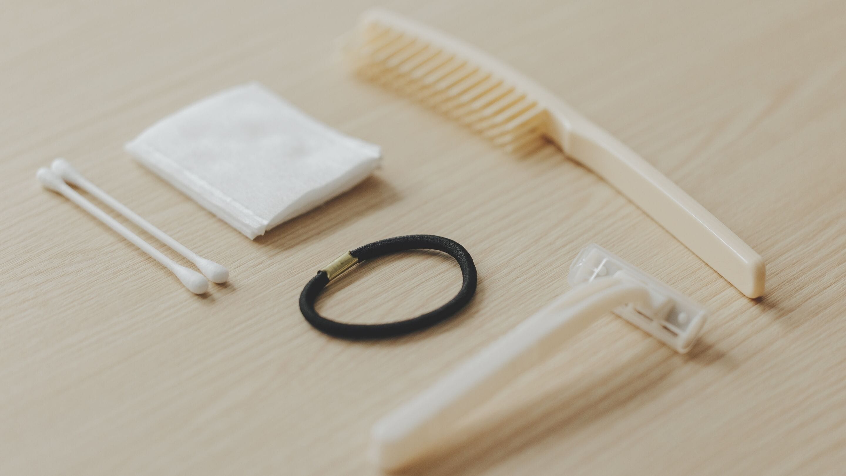 A set of personal care items including cotton swabs, a black hair tie, a white tissue, a wooden comb, and a white toothbrush on a wooden surface.