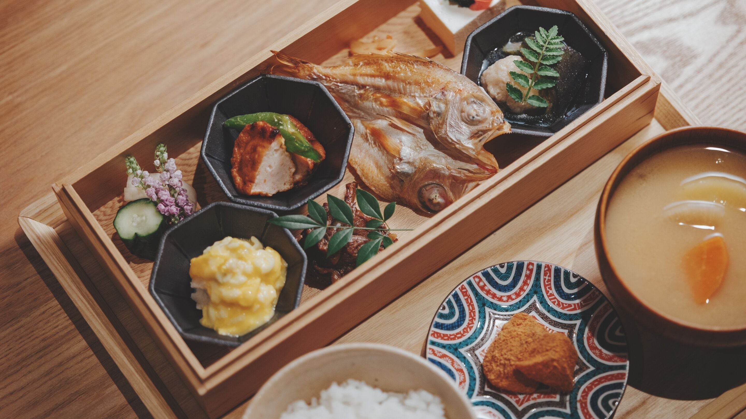 A wooden tray with various dishes including fish, vegetables, and a bowl of soup.