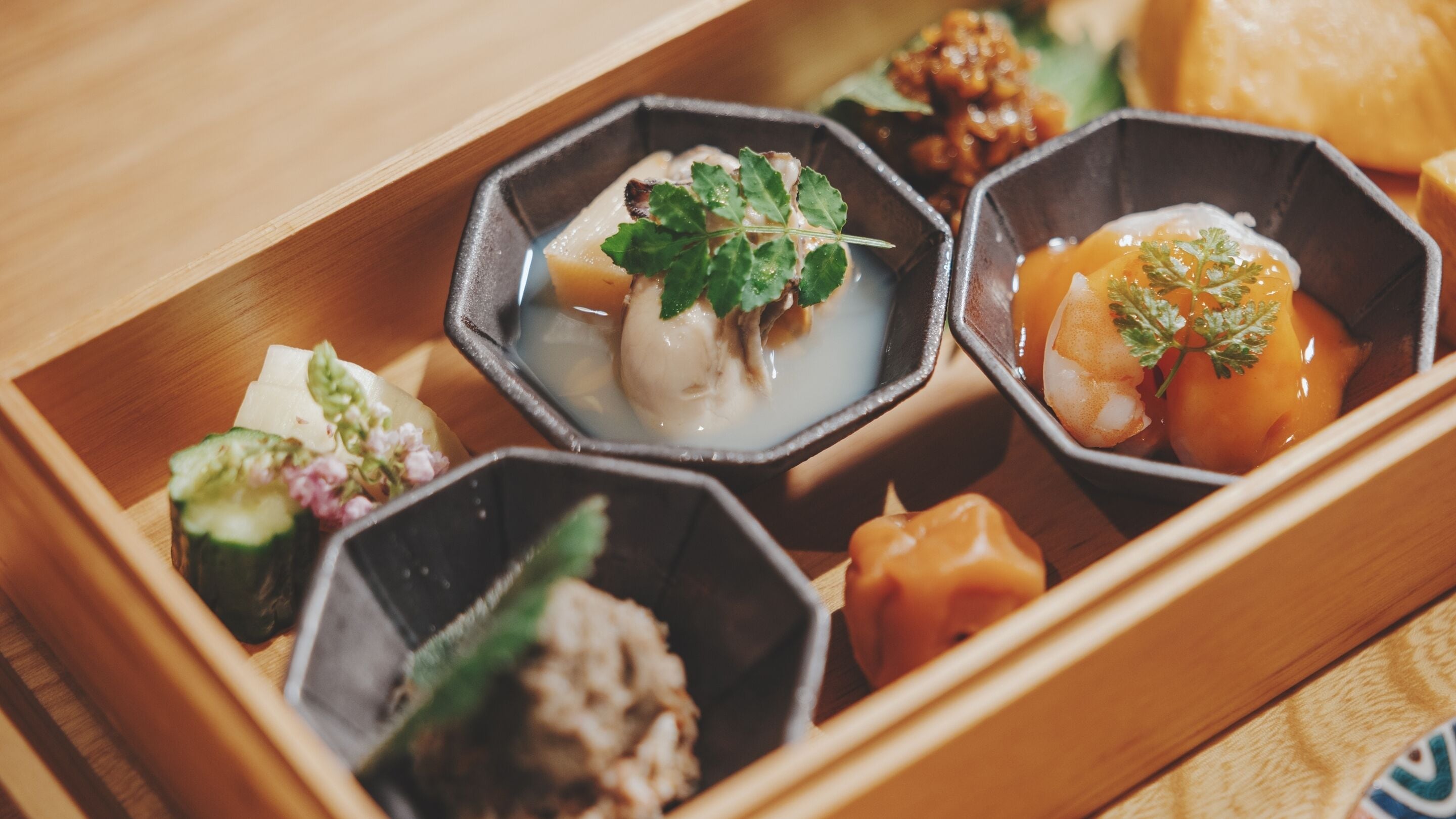 A wooden tray with various food items, including a dish with a leaf garnish.