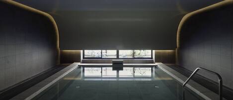 A swimming pool with a view of trees through a window, surrounded by walls with a modern design.