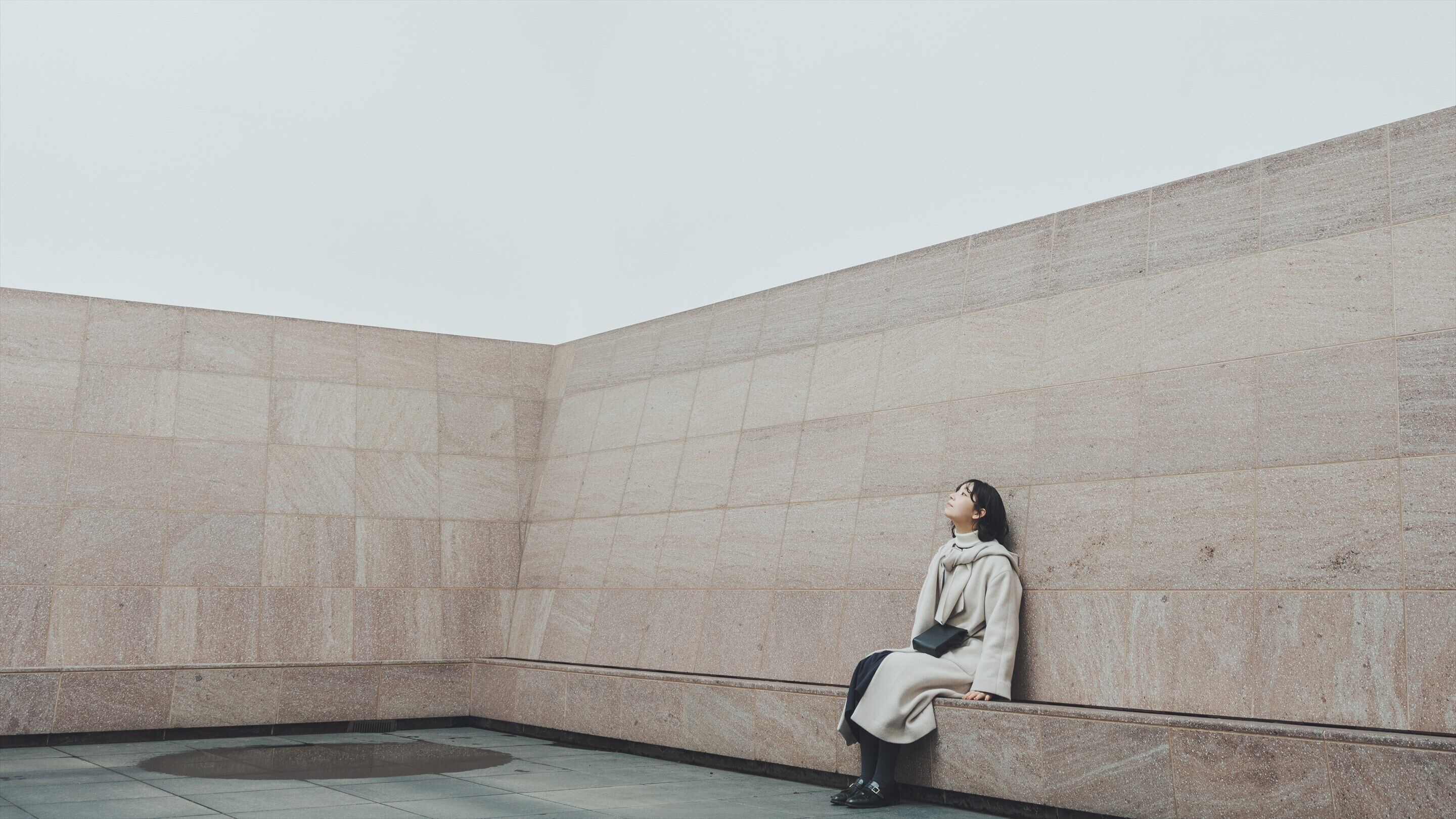 A person sitting on a bench in a room with a plain wall and a tiled floor.