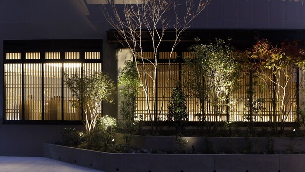 Un edificio moderno con amplios ventanales y un jardín con diversas plantas y árboles.