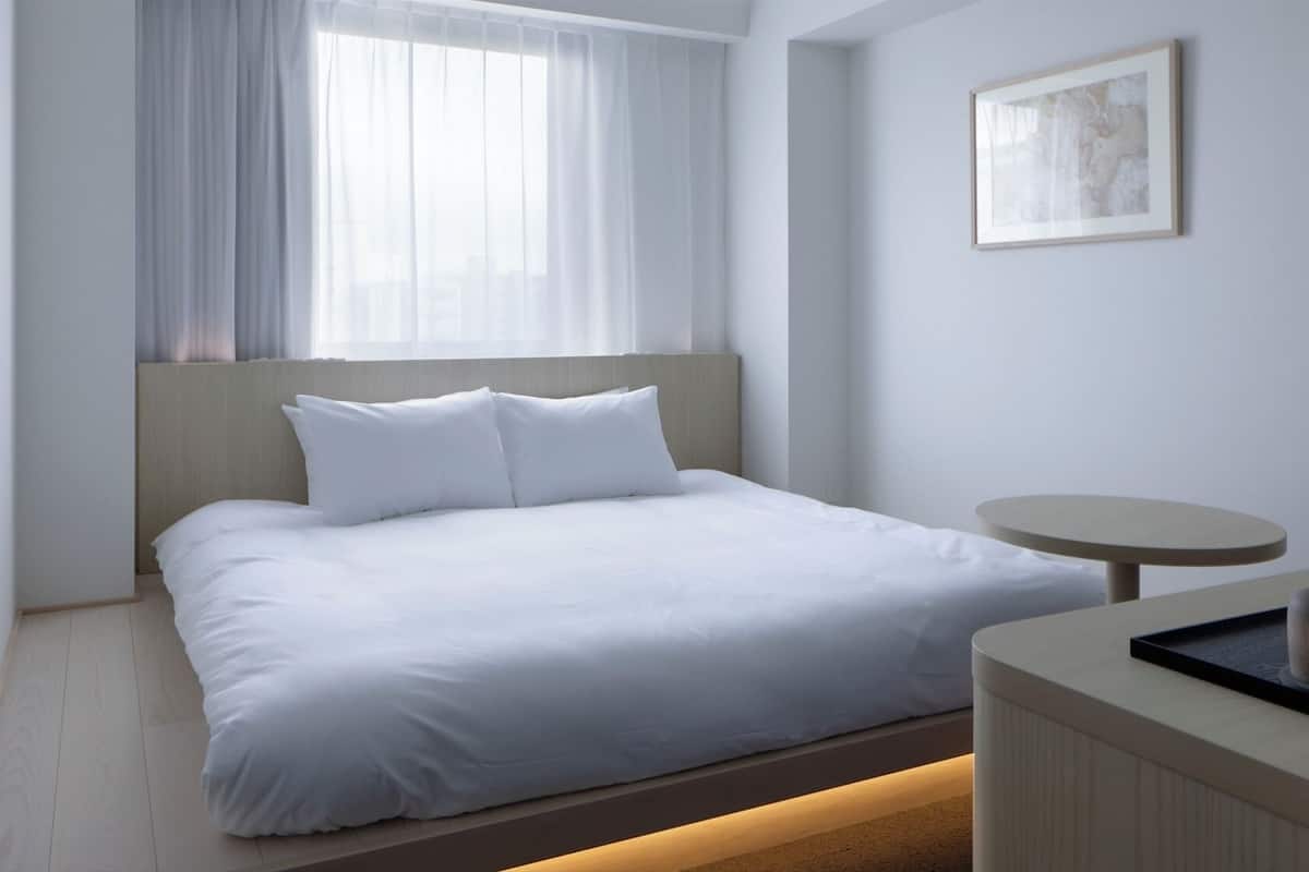 Una habitación de hotel moderna con una cama, una mesa redonda y un ventanal con cortinas translúcidas.