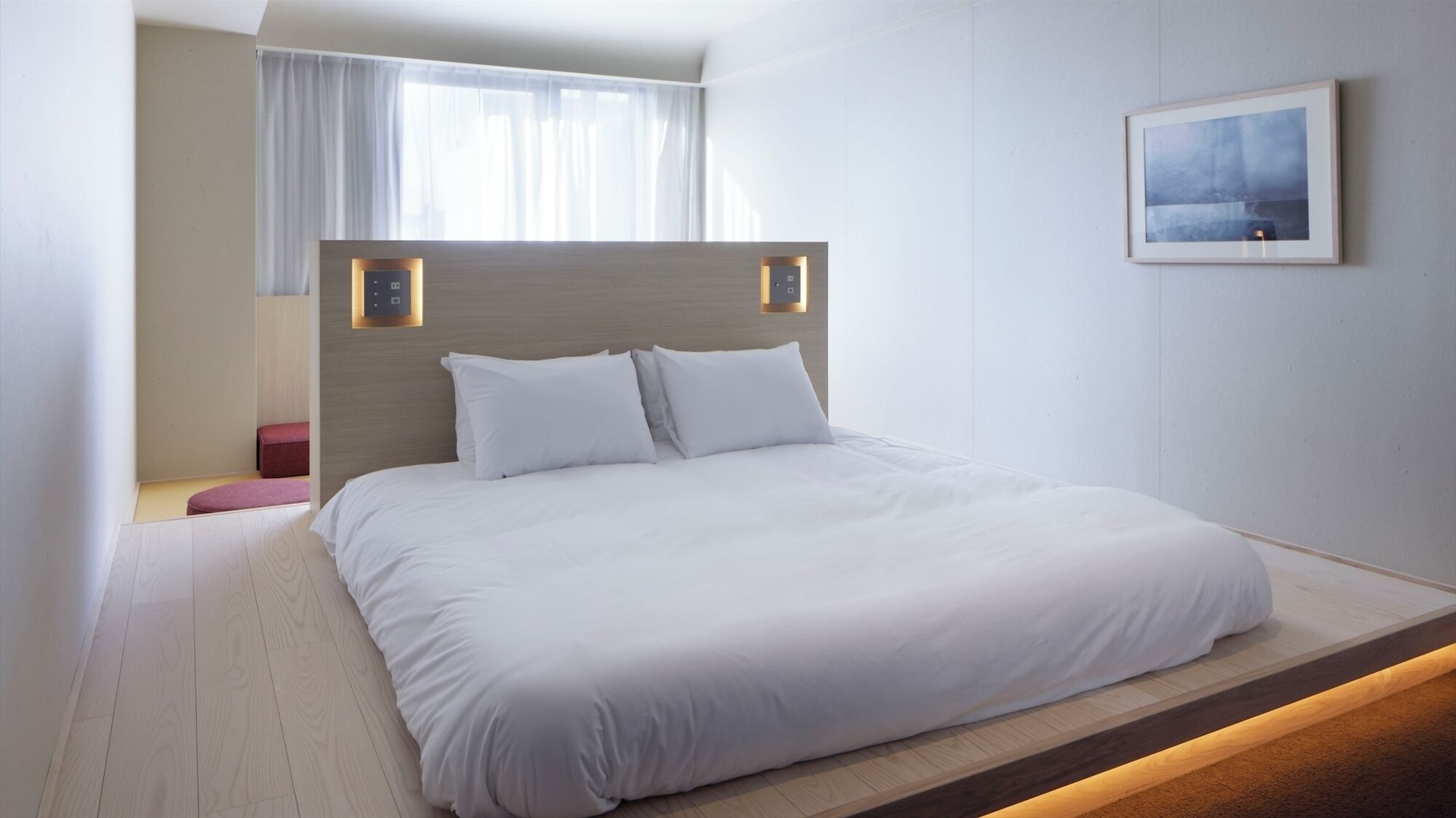 Une chambre d’hôtel moderne avec un grand lit, une tête de lit en bois, un petit coin salon et un tableau encadré au mur.