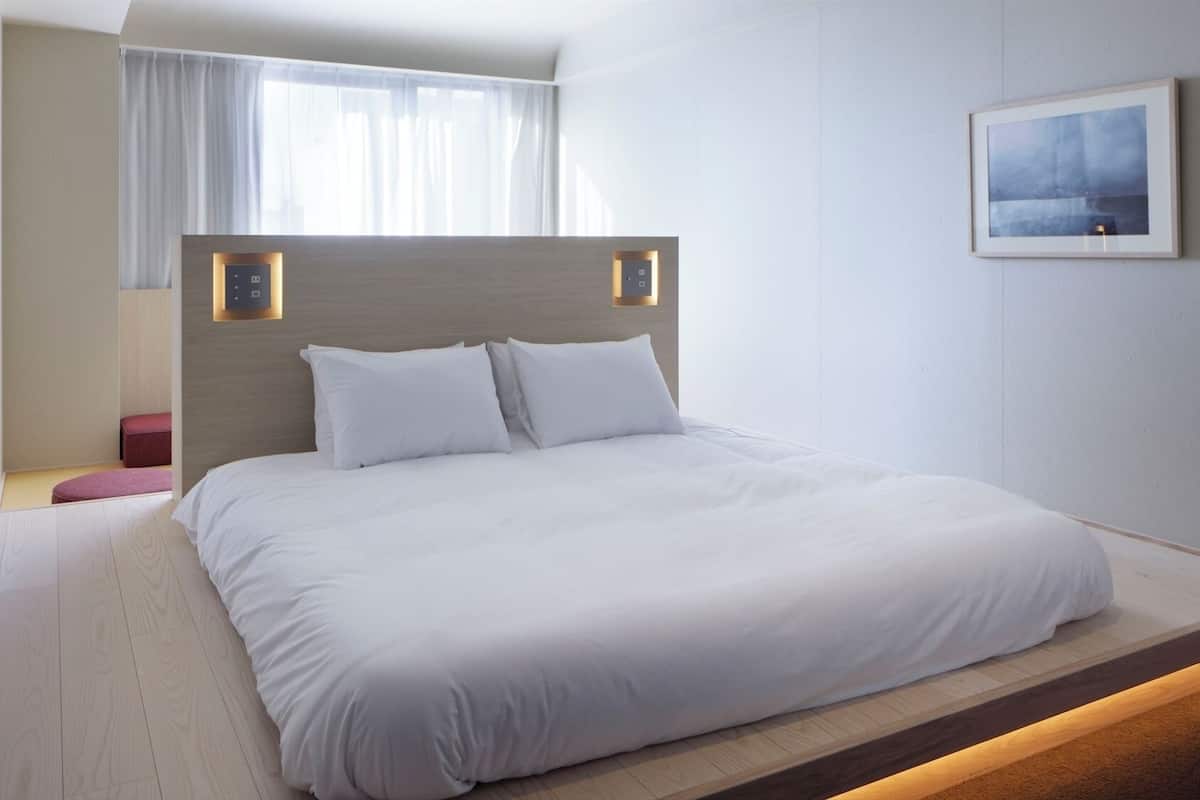 Una habitación de hotel moderna con una cama grande, cabecera de madera, un pequeño espacio para sentarse y un cuadro enmarcado en la pared.