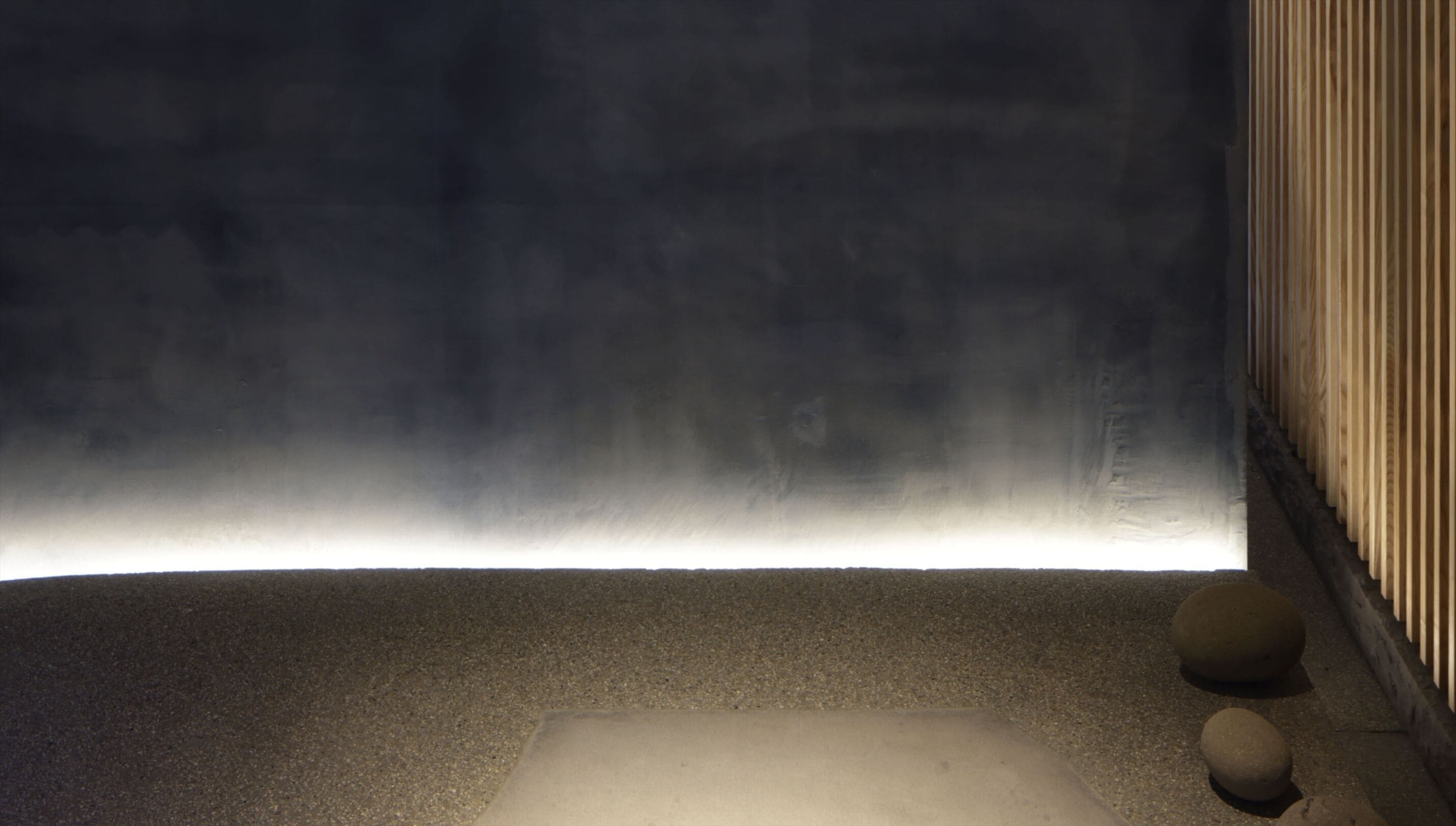 A dark interior space with a smooth, light-colored floor and a vertical wooden panel on the right.