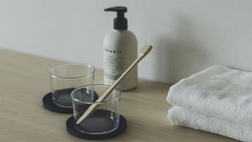 A bathroom with a wooden floor, two clear glasses on black coasters, a white towel, and a bottle of shampoo.