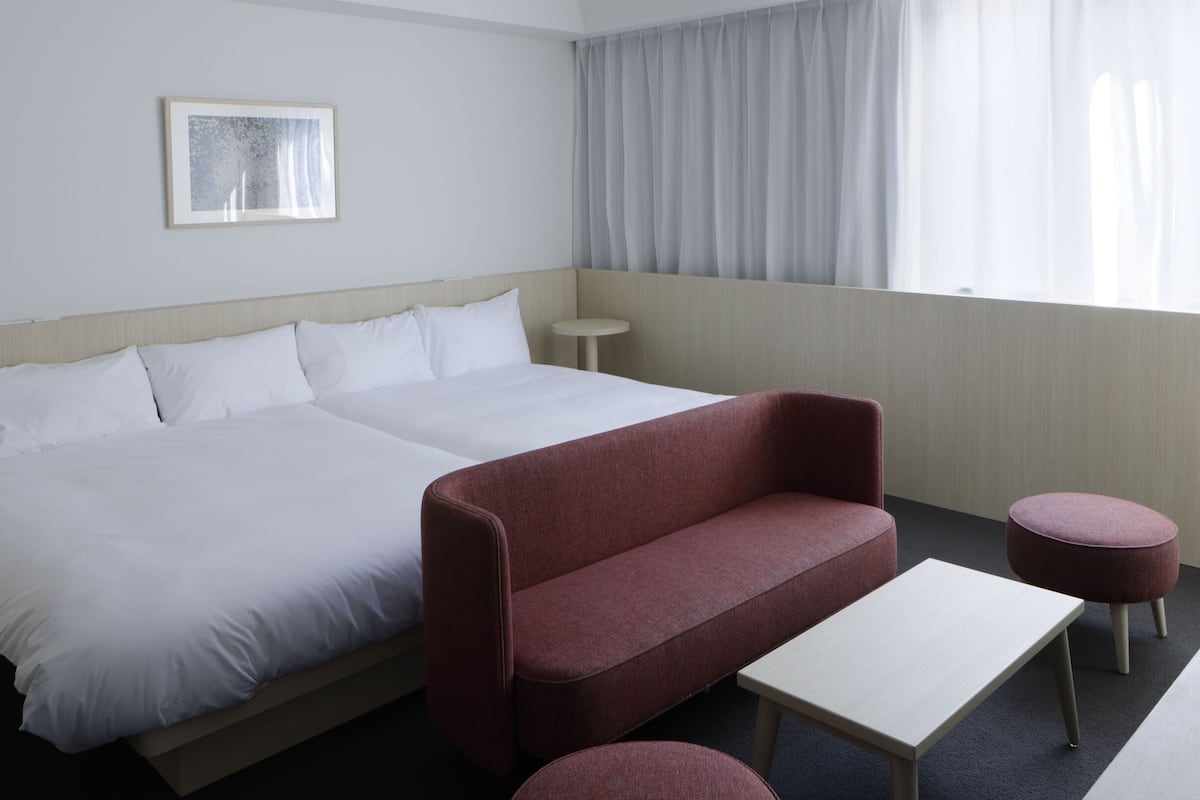 Una habitación de hotel con cama, sofá rojo, una mesita y un reposapiés redondo.