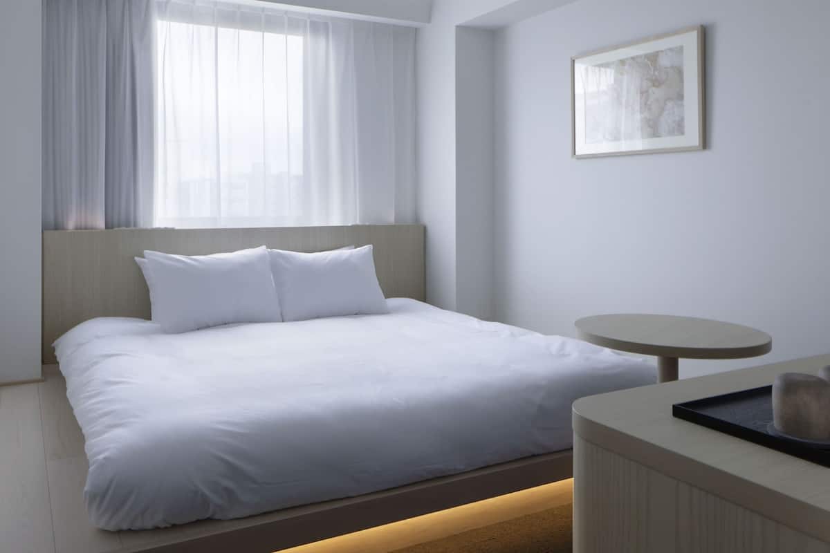 Una habitación de hotel moderna con una cama grande, una mesa redonda y una ventana con cortinas translúcidas.