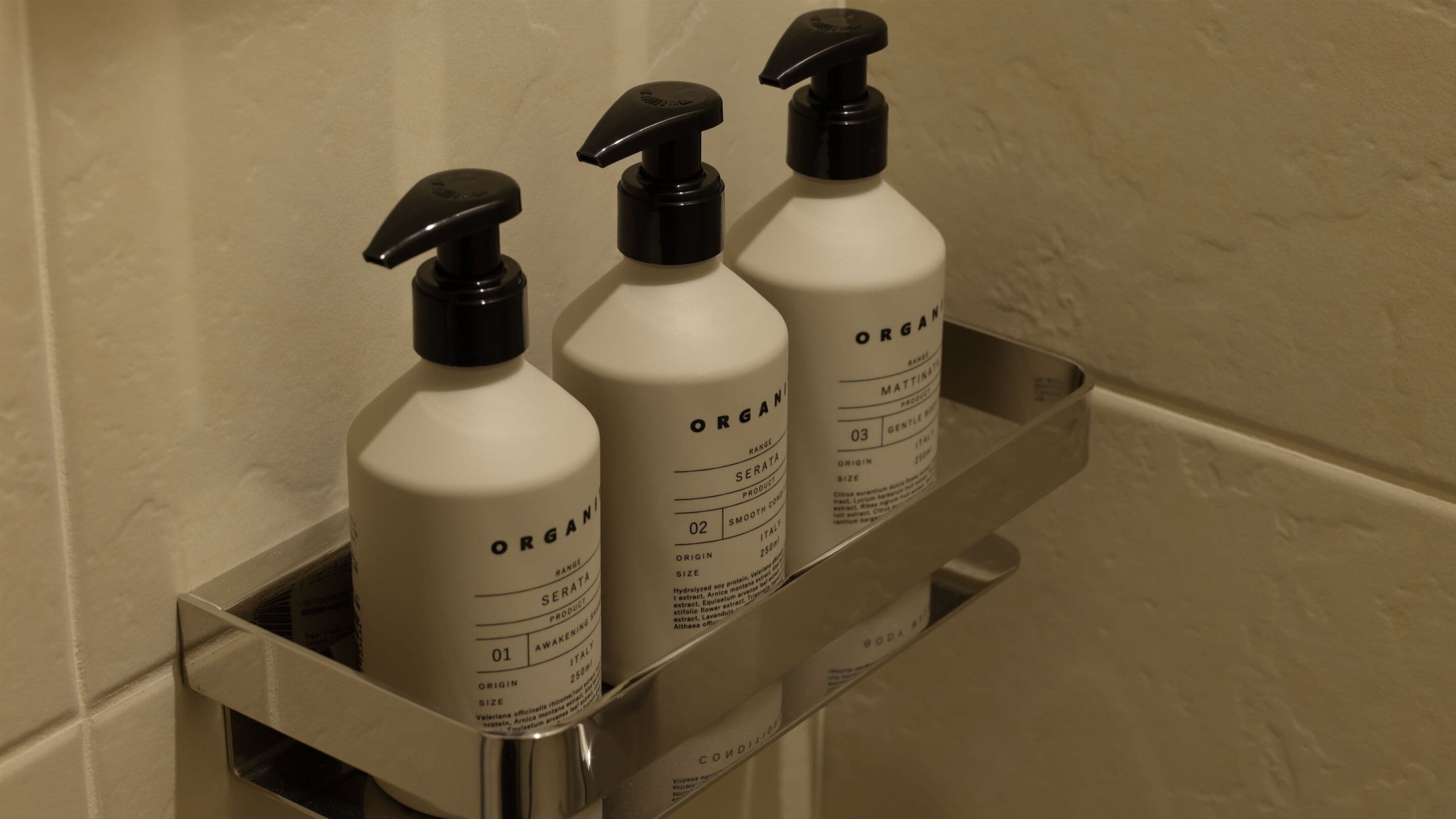 Three bottles of organic skincare products on a metal shelf in a bathroom.