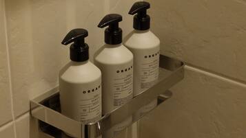Three bottles of organic skincare products on a metal shelf in a bathroom.