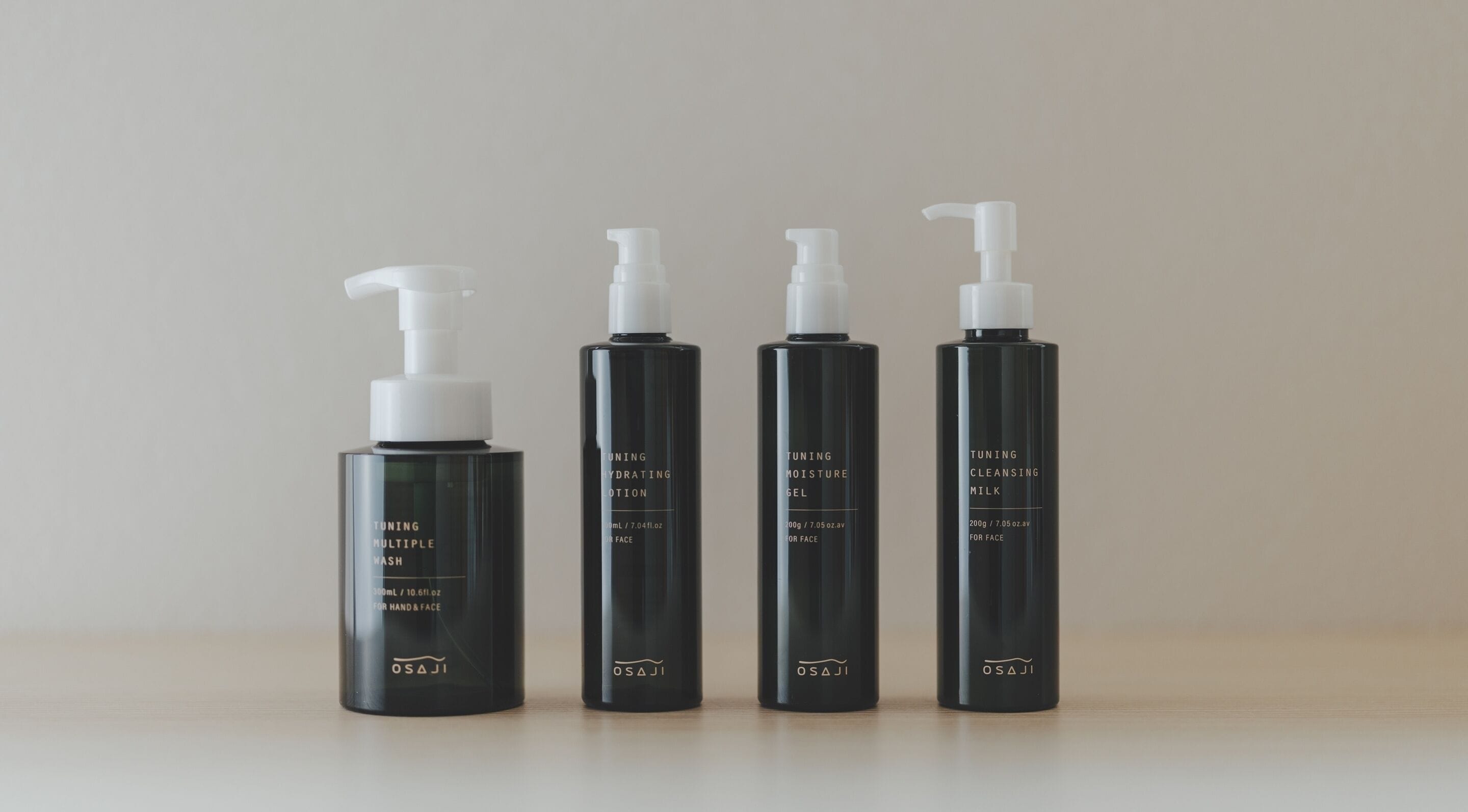 Four black bottles of skincare products with pumps, labeled for different skin types and purposes, arranged on a surface.