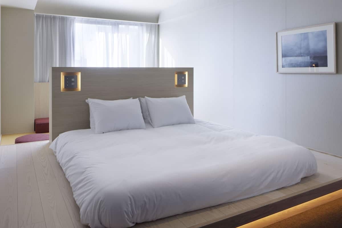 Una habitación de hotel moderna con una cama grande, cabecera de madera, una pequeña zona de estar y un cuadro enmarcado en la pared.