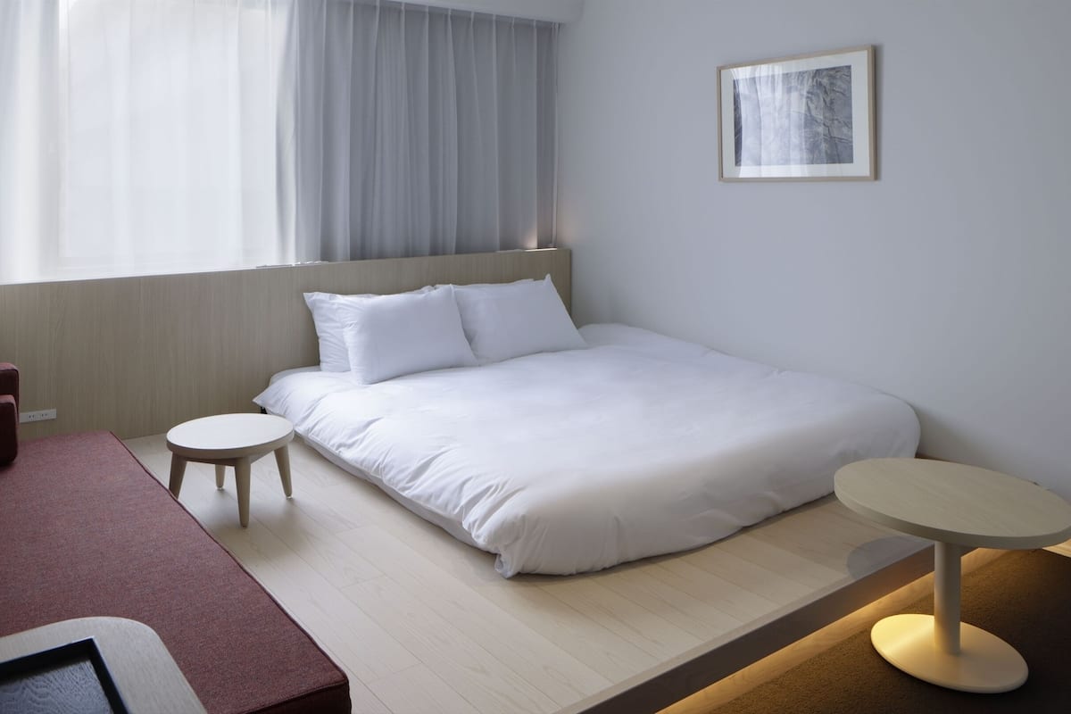 Una habitación de hotel moderna con una cama, una mesita redonda pequeña, un sofá y un cuadro en la pared.