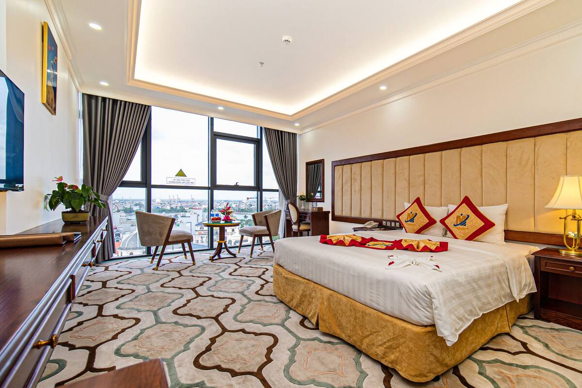 Ein Hotelzimmer mit einem großen Bett, einem Schreibtisch, einem Stuhl und Blick auf die Stadt.