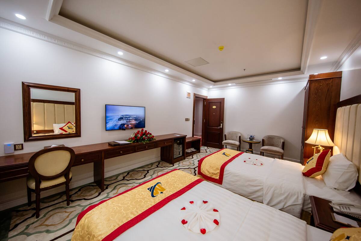 Ein Hotelzimmer mit zwei Betten, einem Schreibtisch, einem Stuhl, einem Fernseher und einem Spiegel.