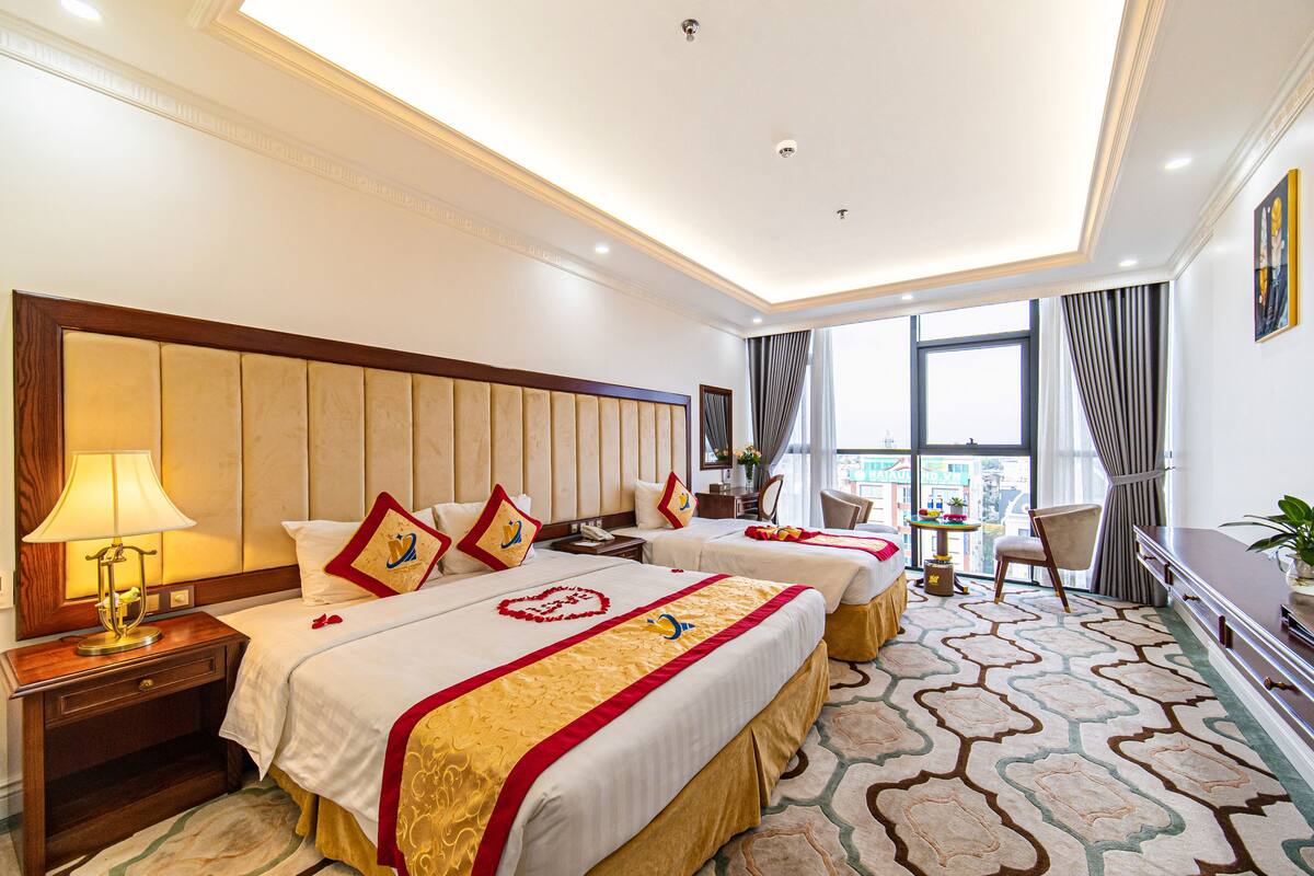 Ein Hotelzimmer mit zwei Betten, einem Schreibtisch, einem Stuhl und Blick auf die Stadt.