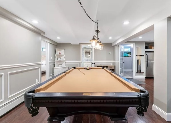 A pool table in a room with white walls and wooden flooring.
