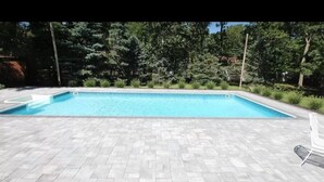 A rectangular swimming pool with a tiled deck, surrounded by greenery and trees. - Perfect summer getaway in Hampton Bays. Last 2 weeks of Summer, still available! (Hampton Bays)