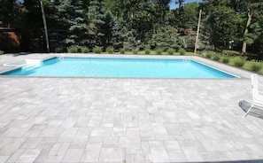 A rectangular swimming pool with a tiled deck, surrounded by greenery and trees. - Perfect summer getaway in Hampton Bays. Last 2 weeks of Summer, still available! (Hampton Bays)