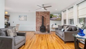 A living room with hardwood flooring, two sofas, a fireplace, and a ceiling fan. - Perfect summer getaway in Hampton Bays. Last 2 weeks of Summer, still available! (Hampton Bays)