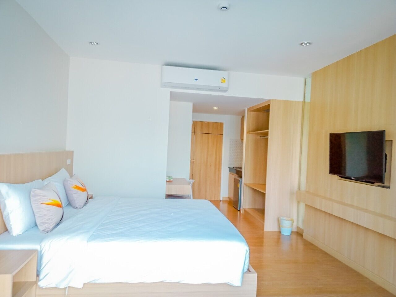 A modern hotel room with a large bed, a TV mounted on the wall, and a wooden wardrobe.