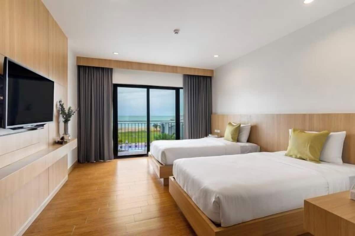 A hotel room with two beds, a TV, a balcony, and a view of the outdoors.