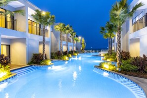 A swimming pool area with a clear view of the pool, surrounded by palm trees and a building with balconies. - Hatchao Heritage Beachfront Resort (Phetchaburi)