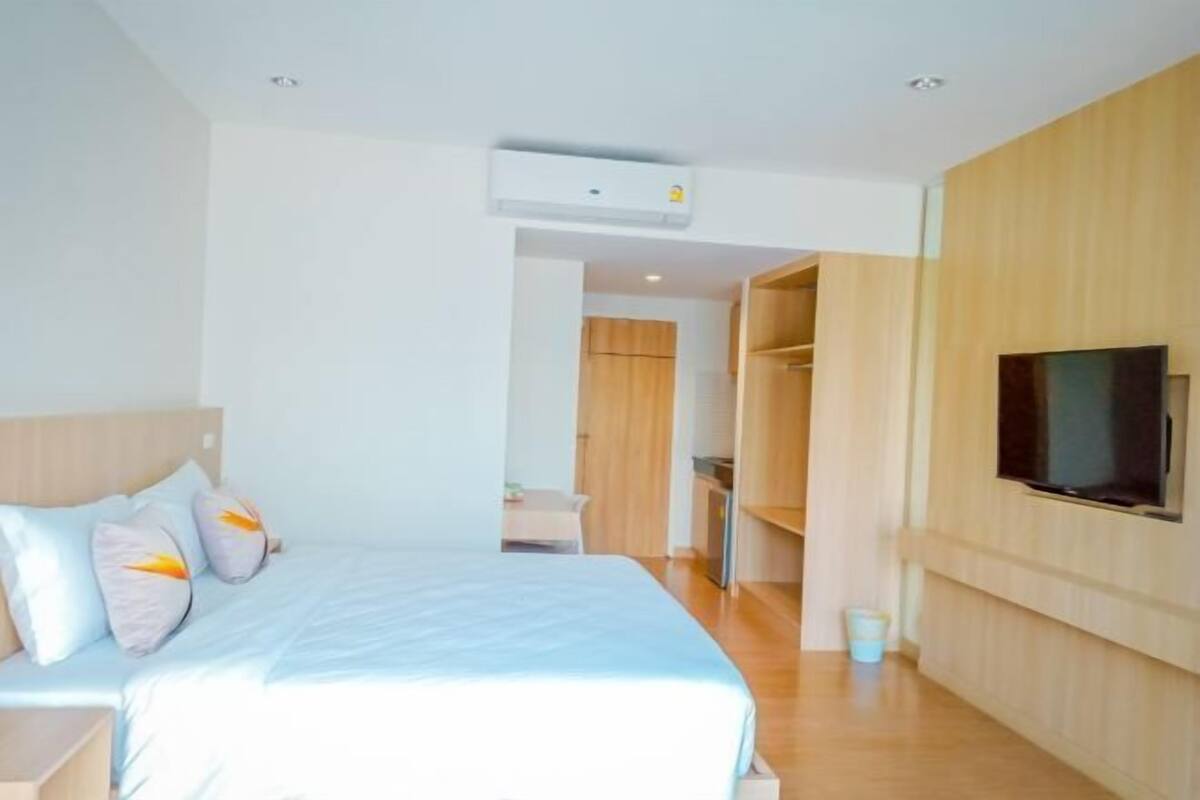 A modern hotel room with a bed, a TV, and a wooden wardrobe.