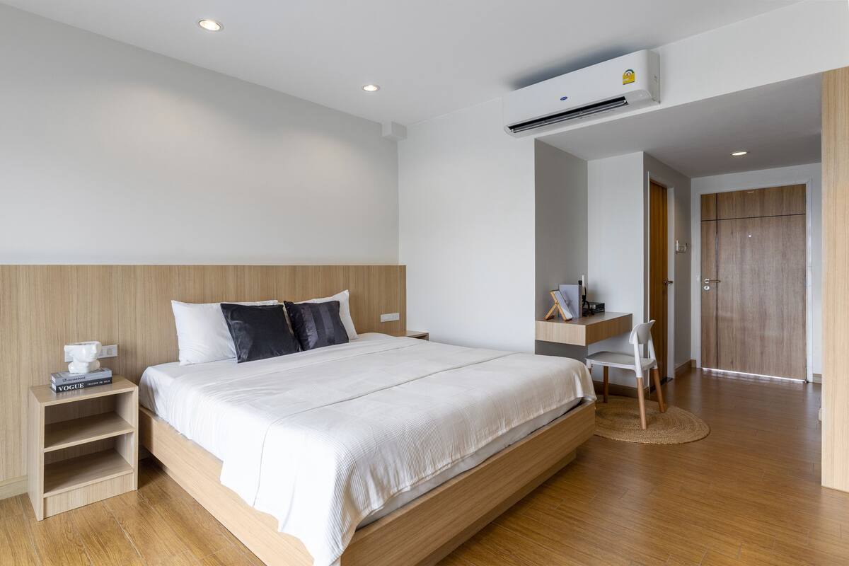 A modern hotel room with a wooden bed, a desk, and an air conditioning unit.