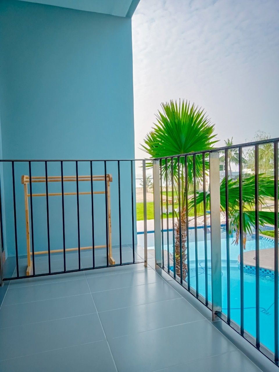 Un balcón con barandilla de metal, una piscina y una palmera.