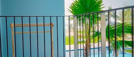 Un balcón con barandilla de metal, una piscina y una palmera.
