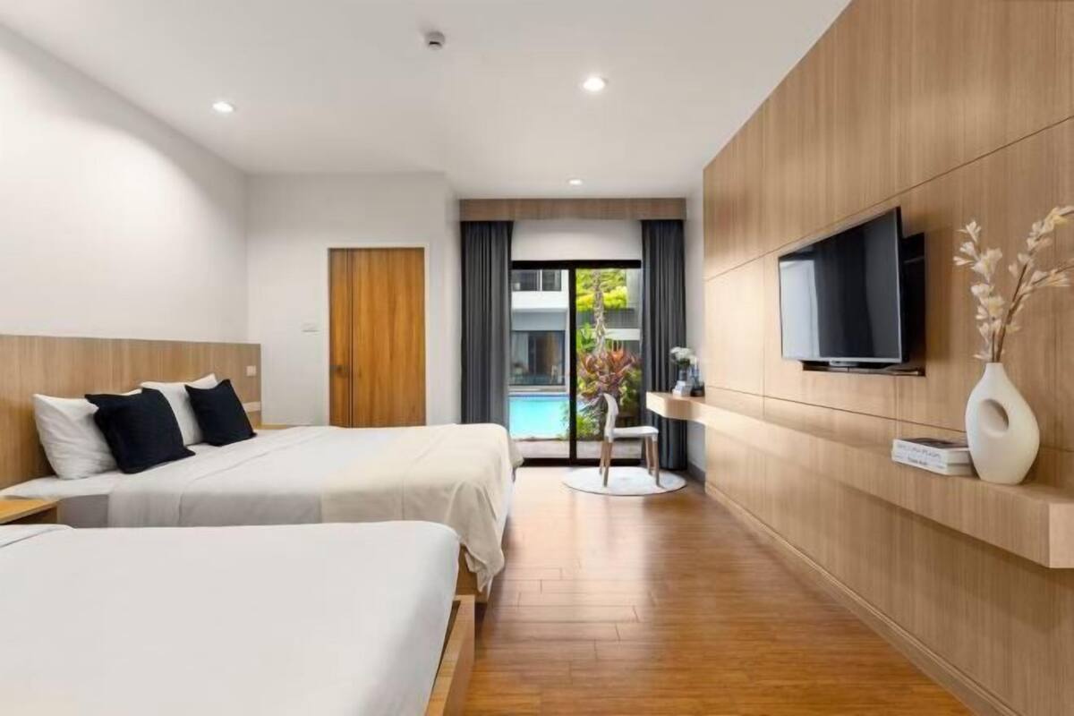 A modern hotel room with two beds, a TV, a small table, and a view of a pool.