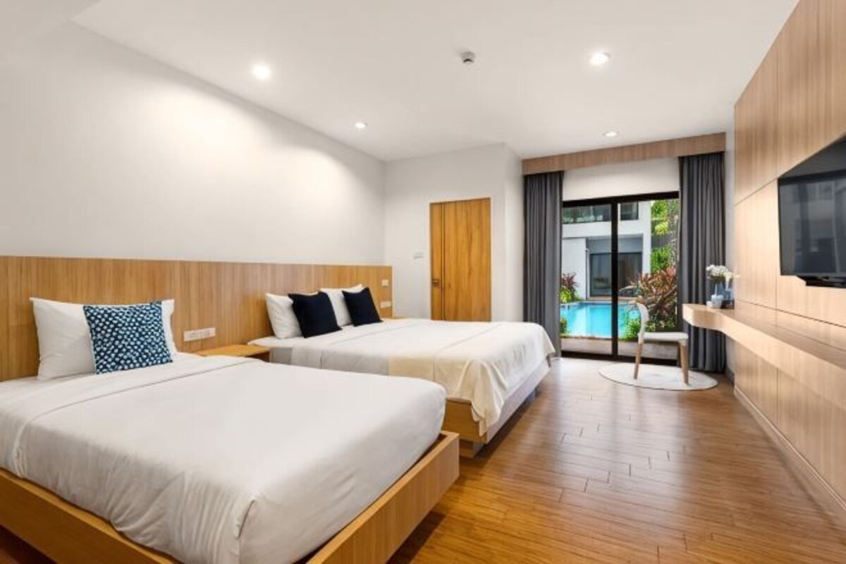 A hotel room with two beds, a wooden floor, a TV, and a view of a swimming pool.