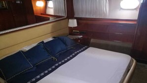 Ein ordentlich bezogenes Bett mit weißer und blauer Bettdecke und passenden Kissen, ein hölzernes Kopfende und ein Nachttisch mit einer Lampe.