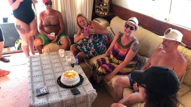 Eine Gruppe von Personen sitzt auf einer Couch und einem Tisch mit Kuchen und Getränken.