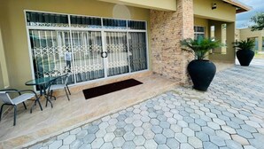 A building with a tiled entrance, a glass door with metal bars, and a small outdoor seating area with chairs. - Ibex Meanwood suite (Lusaka)