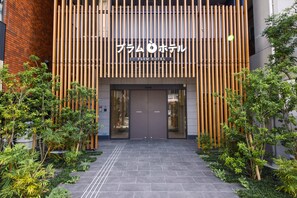 The entrance of Plum Hotel with a modern design, featuring a vertical wooden panel facade and a tiled pathway leading to the entrance. - Plum Hotel (Osaka)