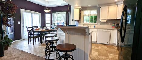 A modern kitchen with white cabinets, a black refrigerator, and a dining area with a table and chairs.