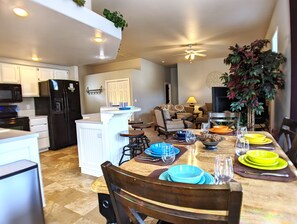 A modern kitchen with a central island, dining table set with plates and glasses, and a living area with a sofa and chairs.