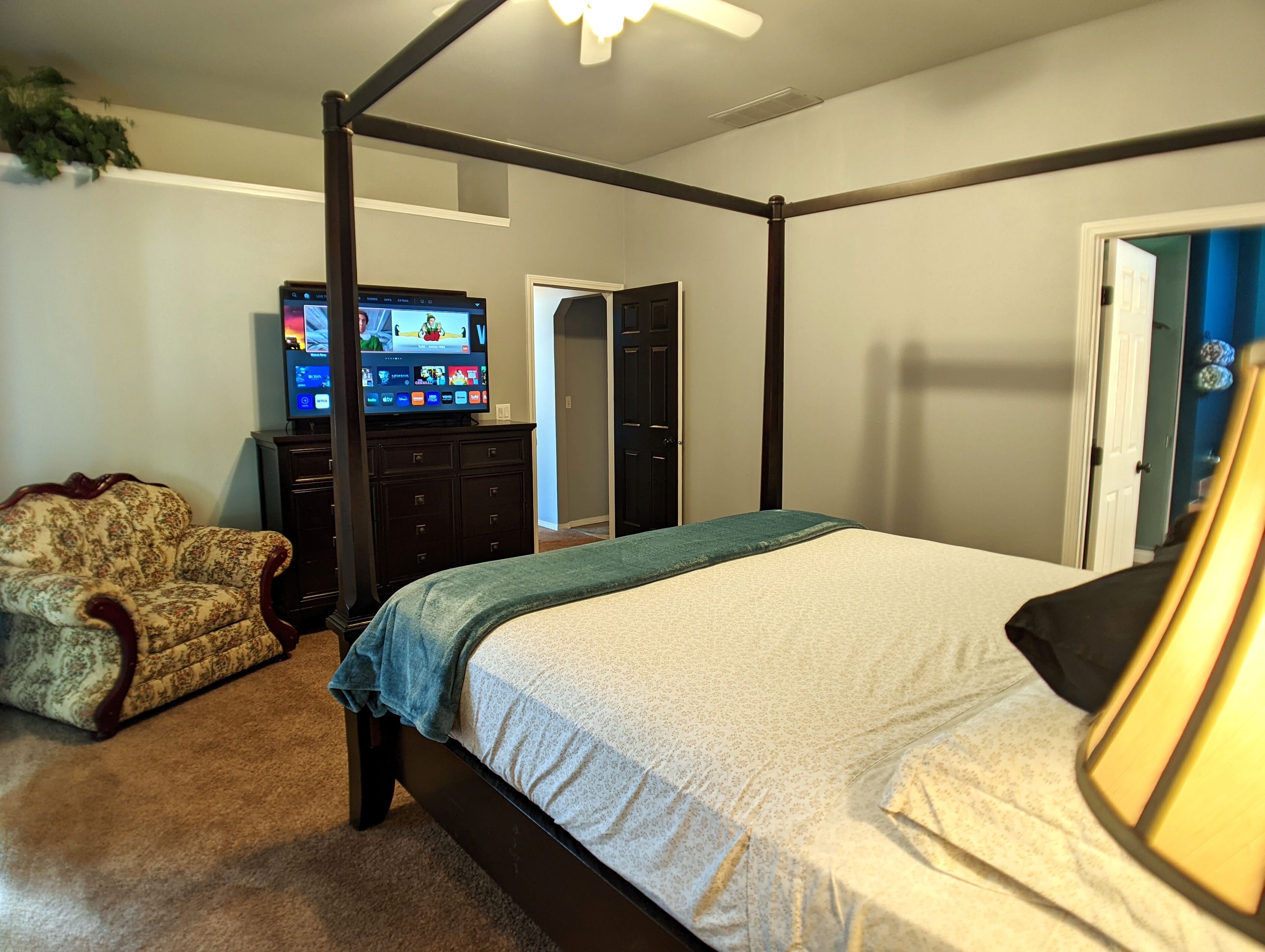 A bedroom with a four-poster bed, a television on a dresser, and a chair.