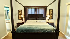 Una cama con dosel de madera oscura, dos mesitas de noche con lámparas y una ventana con cortinas.