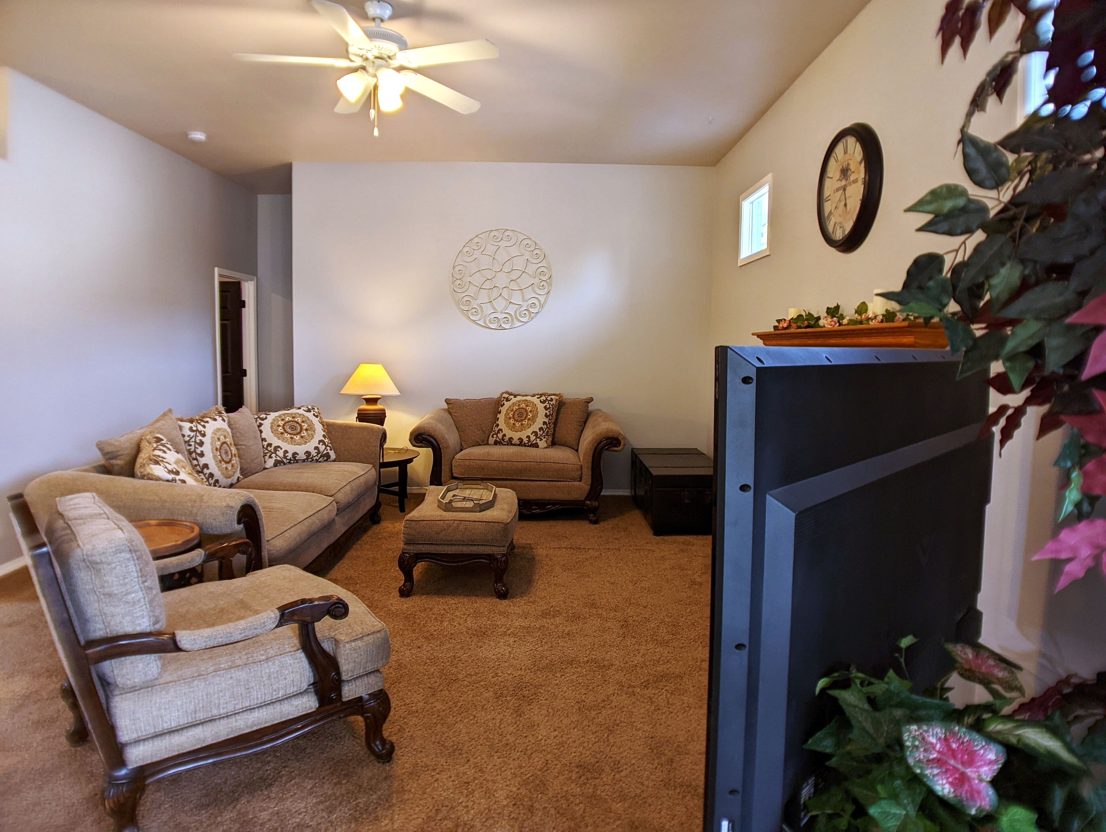A living room with a ceiling fan, a clock, and a television.
