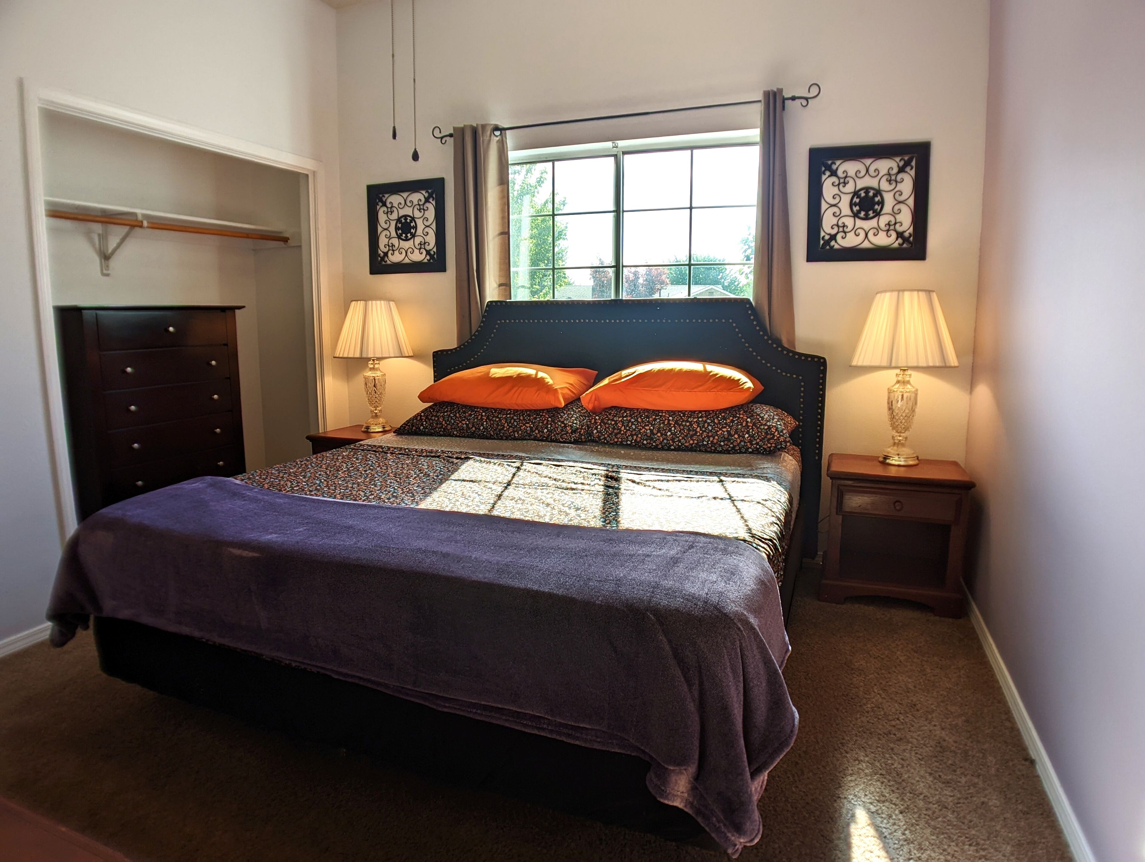 Een slaapkamer met een bed, twee bedlampen, een dressoir en twee kunstwerken aan de muur.