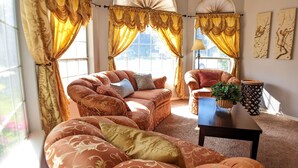 Una sala de estar con un sofá, una mesa de centro y una lámpara. Hay cortinas y un ventanal con vistas.