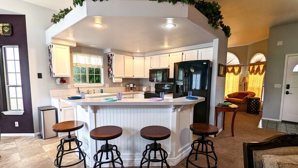 Una cocina moderna con armarios blancos, un refrigerador negro y una isla central con taburetes.