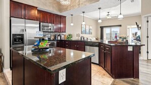 A modern kitchen with dark wood cabinets, stainless steel appliances, and a large granite island.